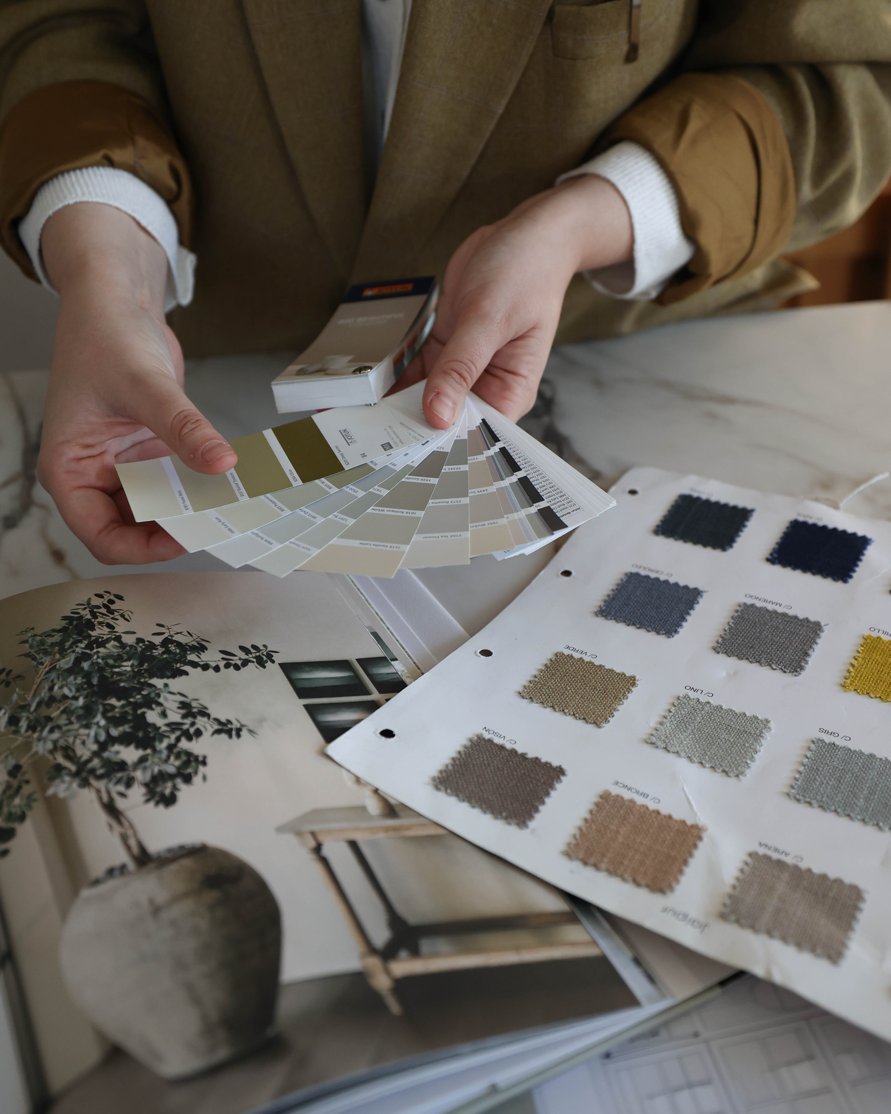 Manos sosteniendo una carta de colores junto a muestras de tejidos y catálogos de interiorismo