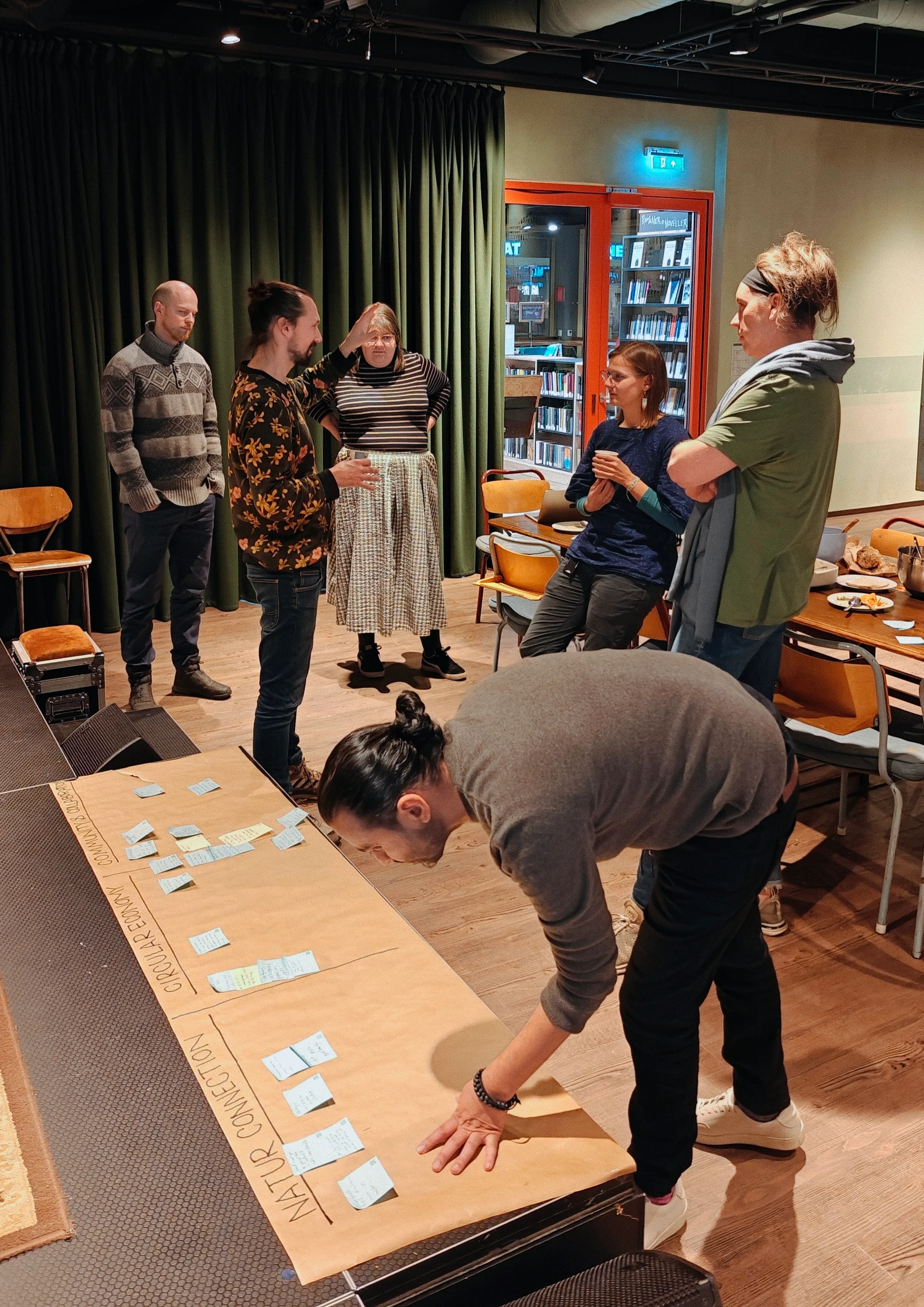 People talking in a room and one person putting down sticky notes on a board