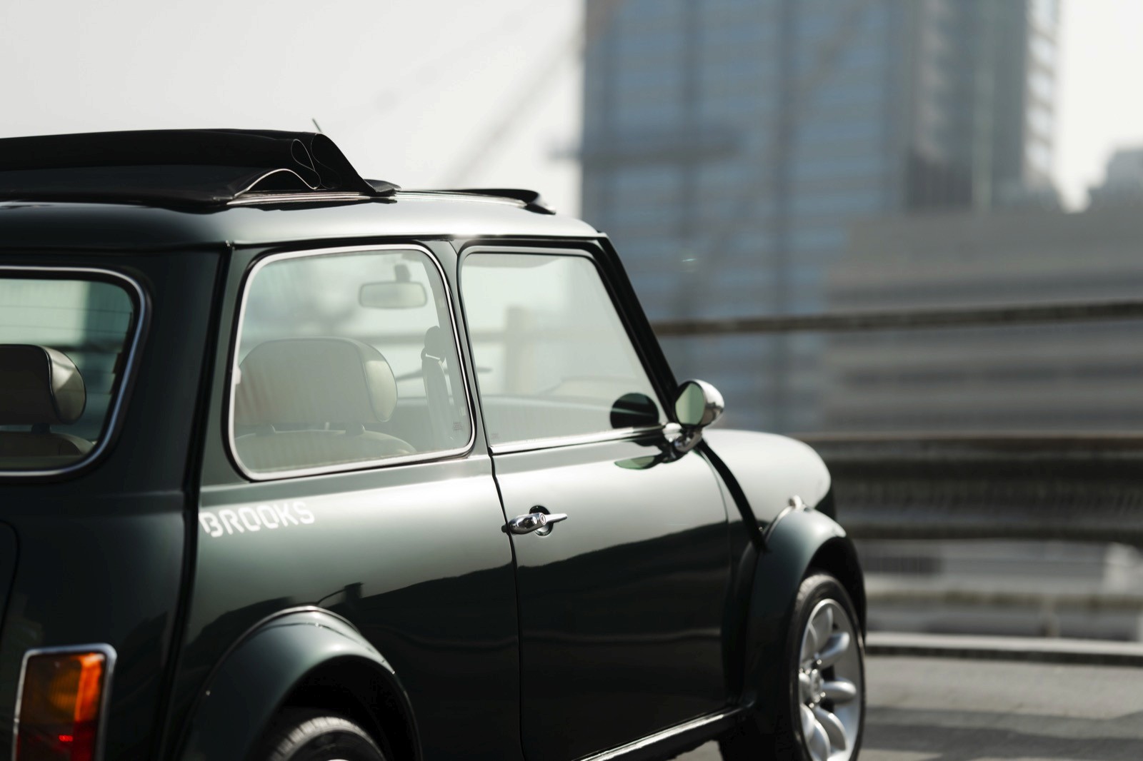 A close-up of a green car parked, showing its rear and side mirrors, against an industrial background.