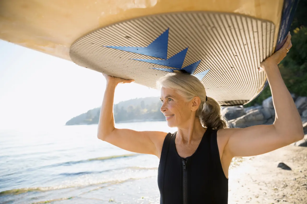 Mujer sonriendo al sol en la playa realizando surf: seguros con enfermedad previa y derecho al olvido oncológico
