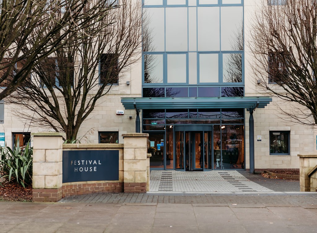 Main entrance of the dermatology clinic at Festival House, Cheltenham, featuring a modern glass facade and revolving door.