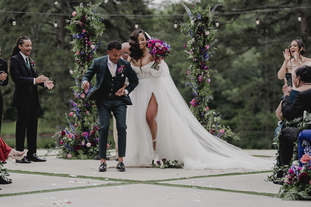 Newlyweds walking through a floral ceremony installation beneath string lights.