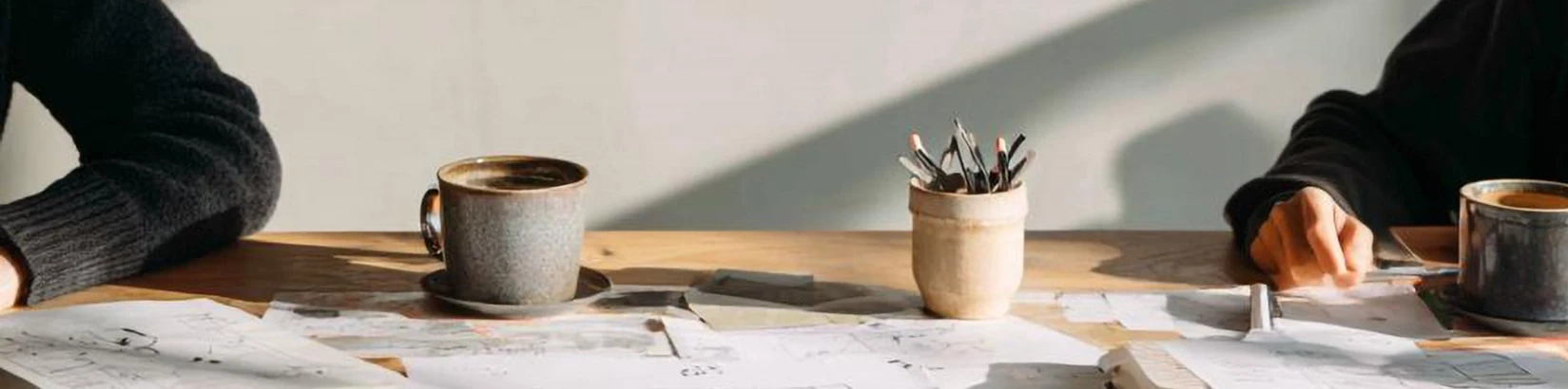 A cozy and professional collaborative workspace in a product design studio, featuring sketches, coffee mugs, and design drafts on a wooden table, inviting founders to start their SaaS journey