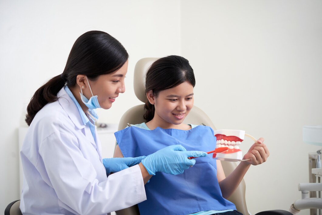 A dental professional showing a dental model to a young patient, explaining dental procedures and care.