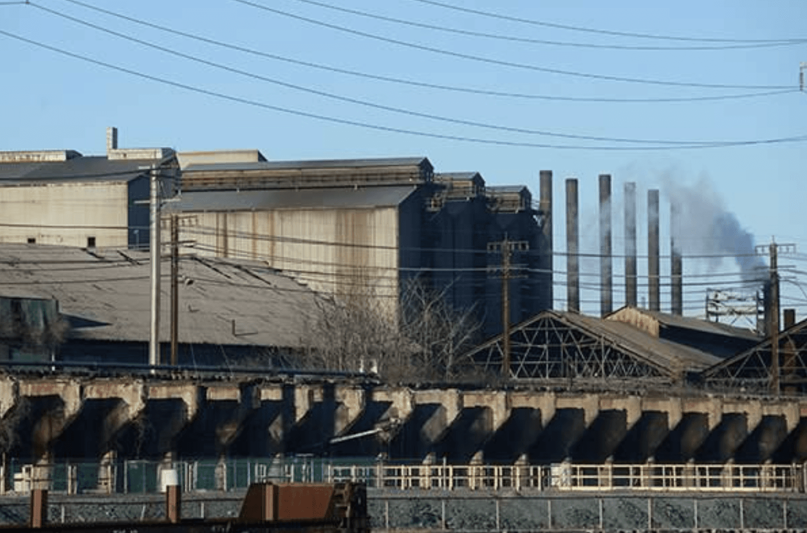 The image depicts an industrial factory with multiple smokestacks against a clear sky.