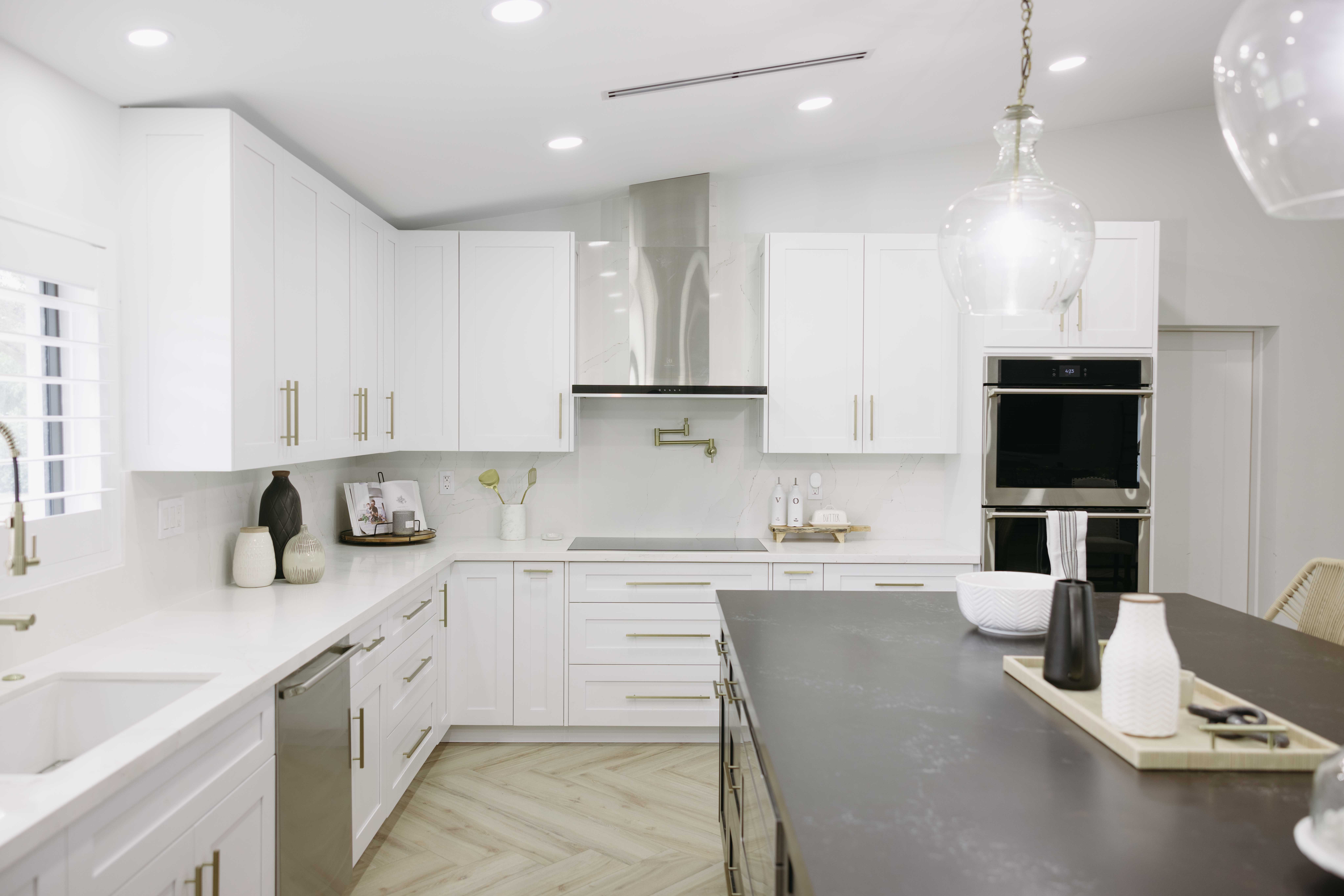 Modern white kitchen with island, stainless steel appliances, and herringbone floor.