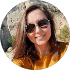 Close-up portrait of a blonde woman in translucent pink glasses and a white shirt on a soft blue background.