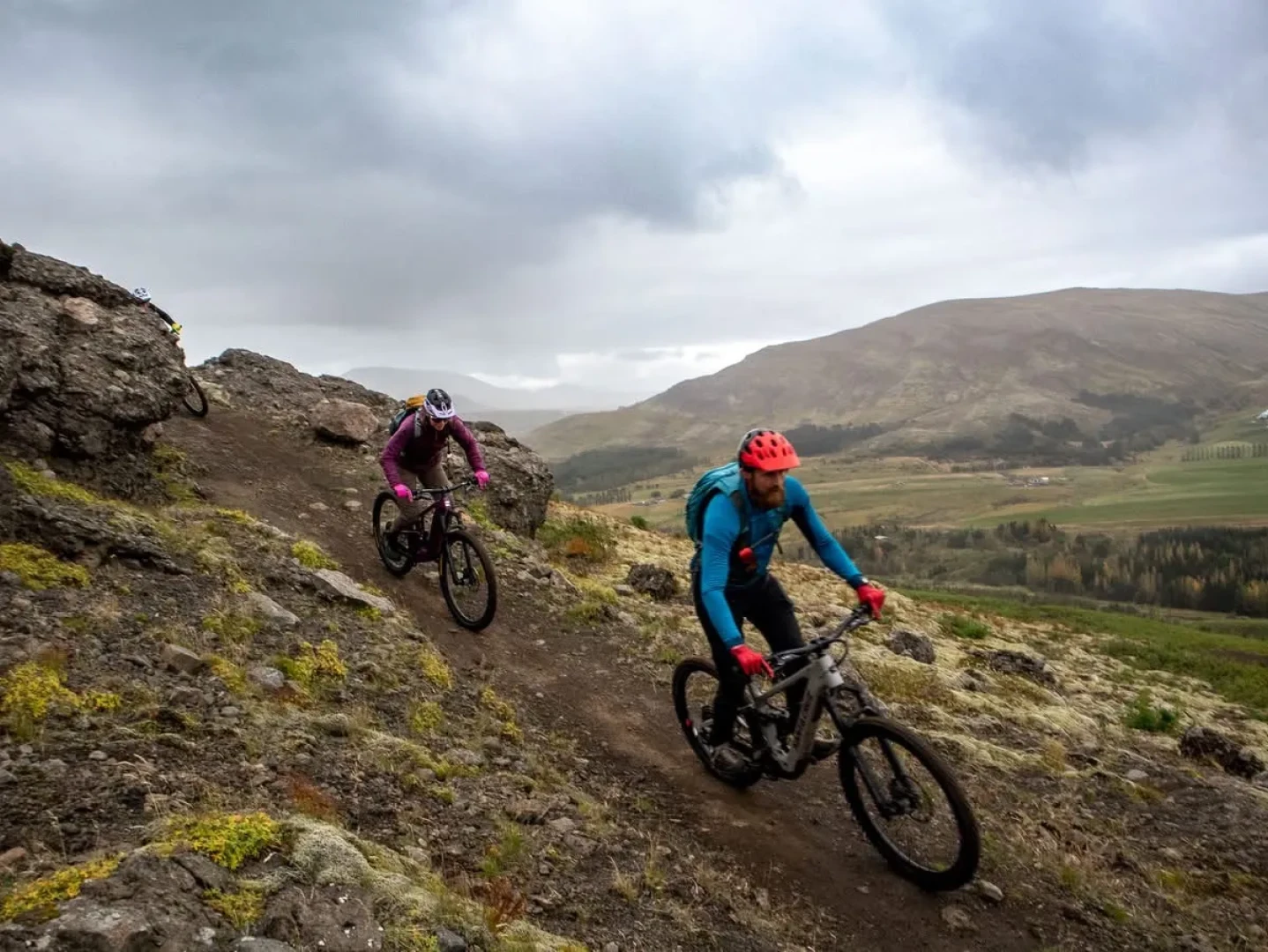man and woman ride mountainbikes down a mountain