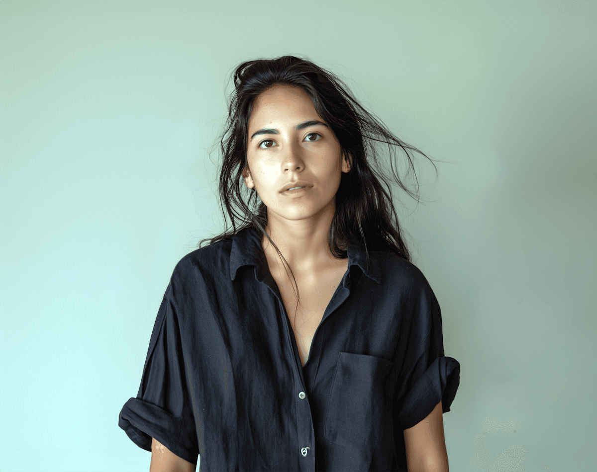 A woman with curly dark hair and a beige shirt stands in soft natural light, creating a serene and minimalistic portrait. professional neutral portrait photo for profile or avatar use .clean, neutral office avatar photo with natural light and simple background