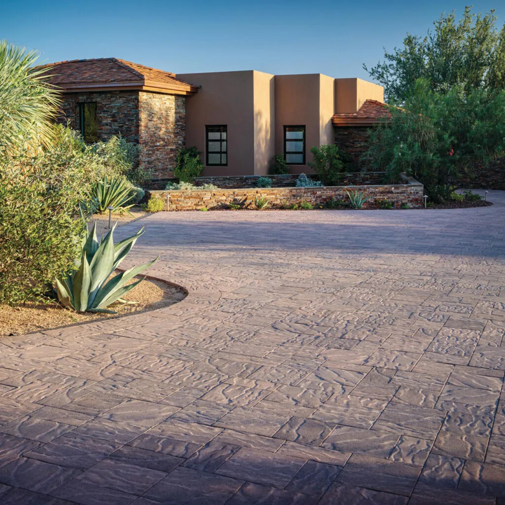Textured driveway curving past a stucco home and planted borders.