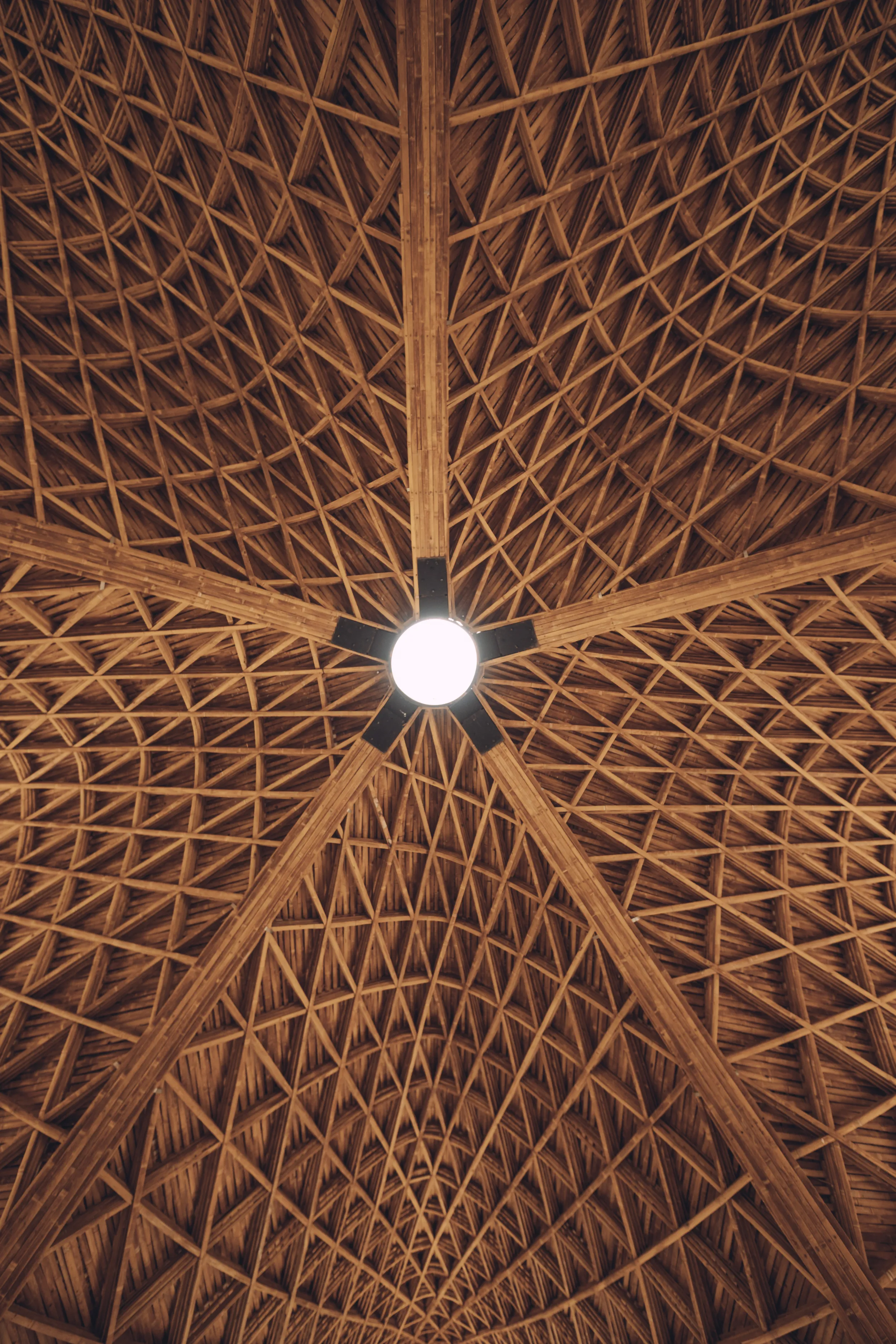 Looking up at the central oculus of Luum Temple's ceiling, showing the converging bamboo beams and intricate parametric weaving pattern.