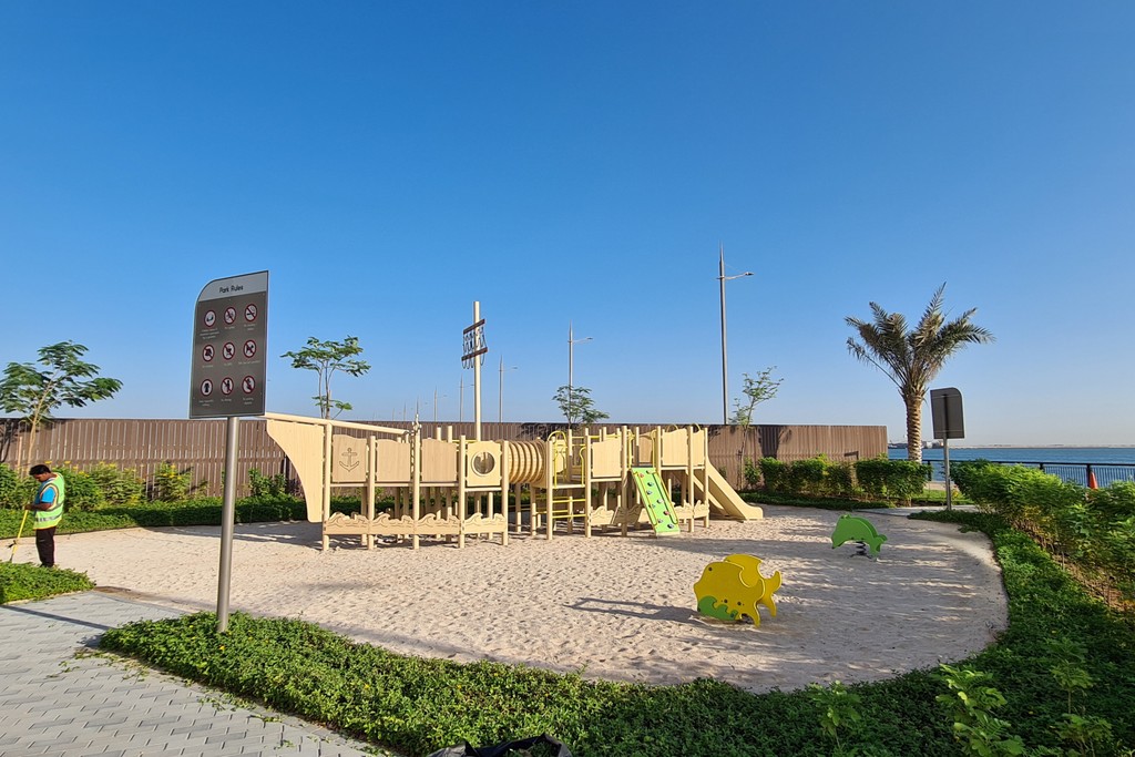 A panoramic image of Dubai Maritime City park with well-maintained lawns, trees, and urban structures surrounding the area.