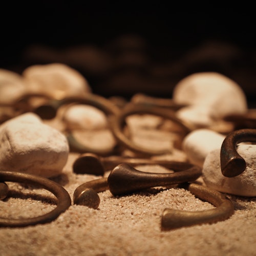 戒指和圆柱形物体静卧在沙质表面上，四周是白色石头，背景为深色。