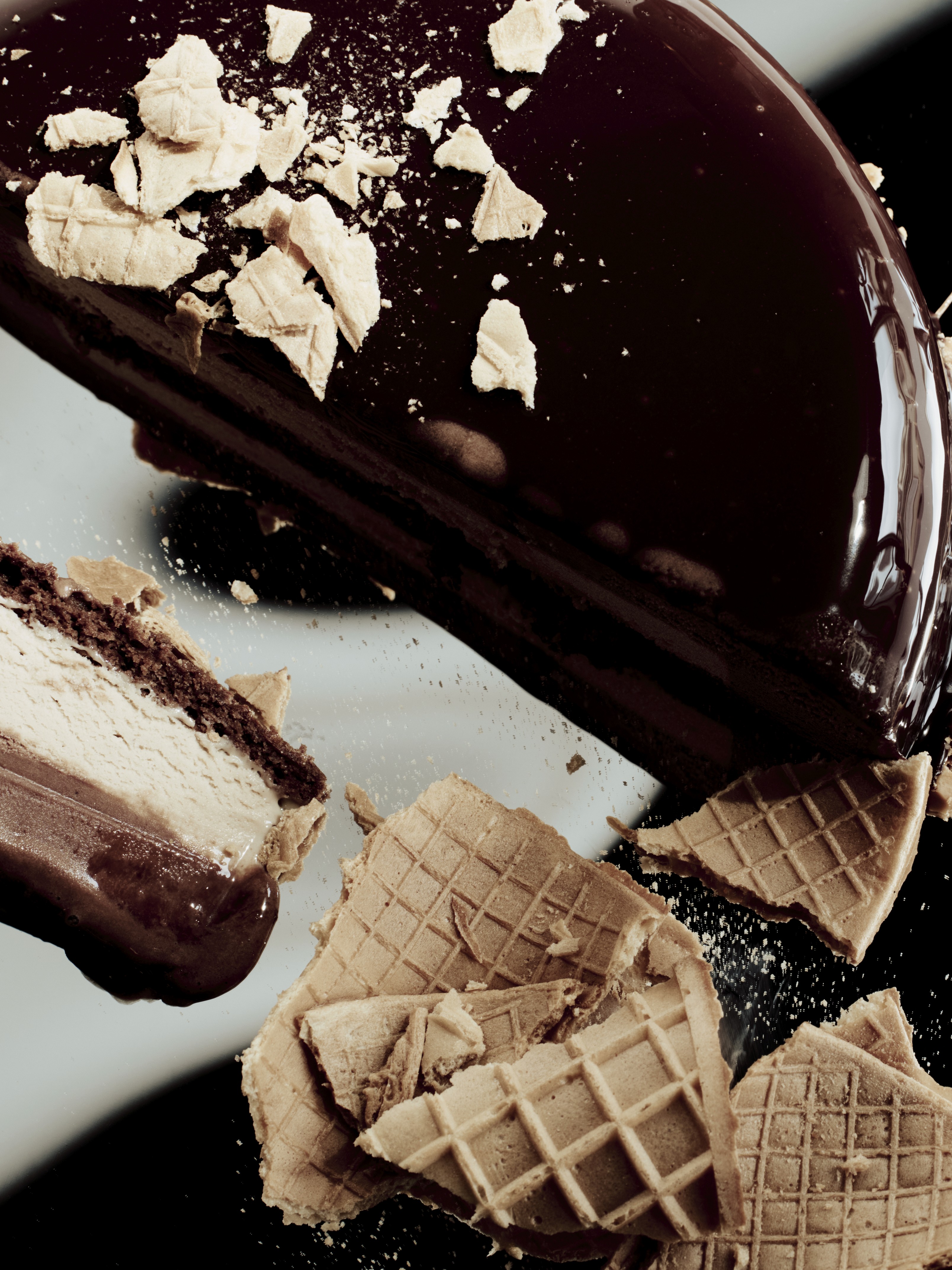 Gâteau glacé au chocolat brillant, partiellement découpé, entouré de morceaux de gaufrette croustillante
