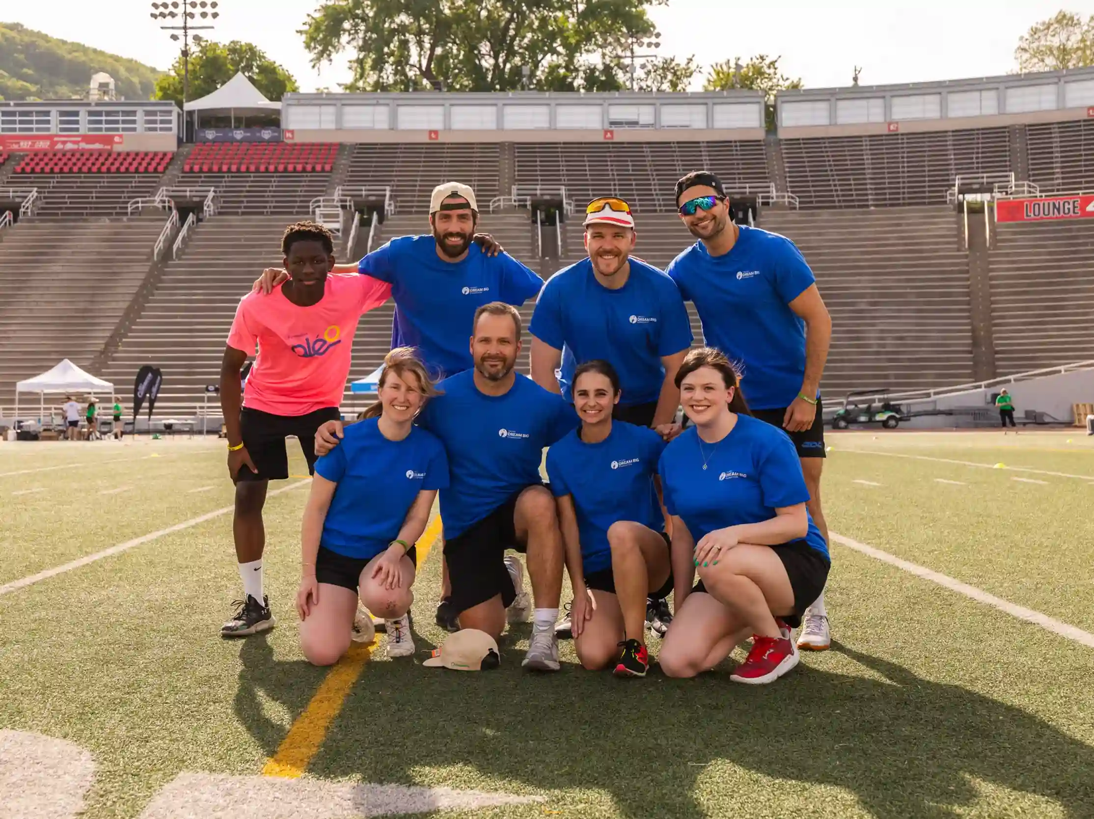 Valsef Dream Big Foundation team poses on the field at a charity event with a young participant in a pink Oléo shirt.