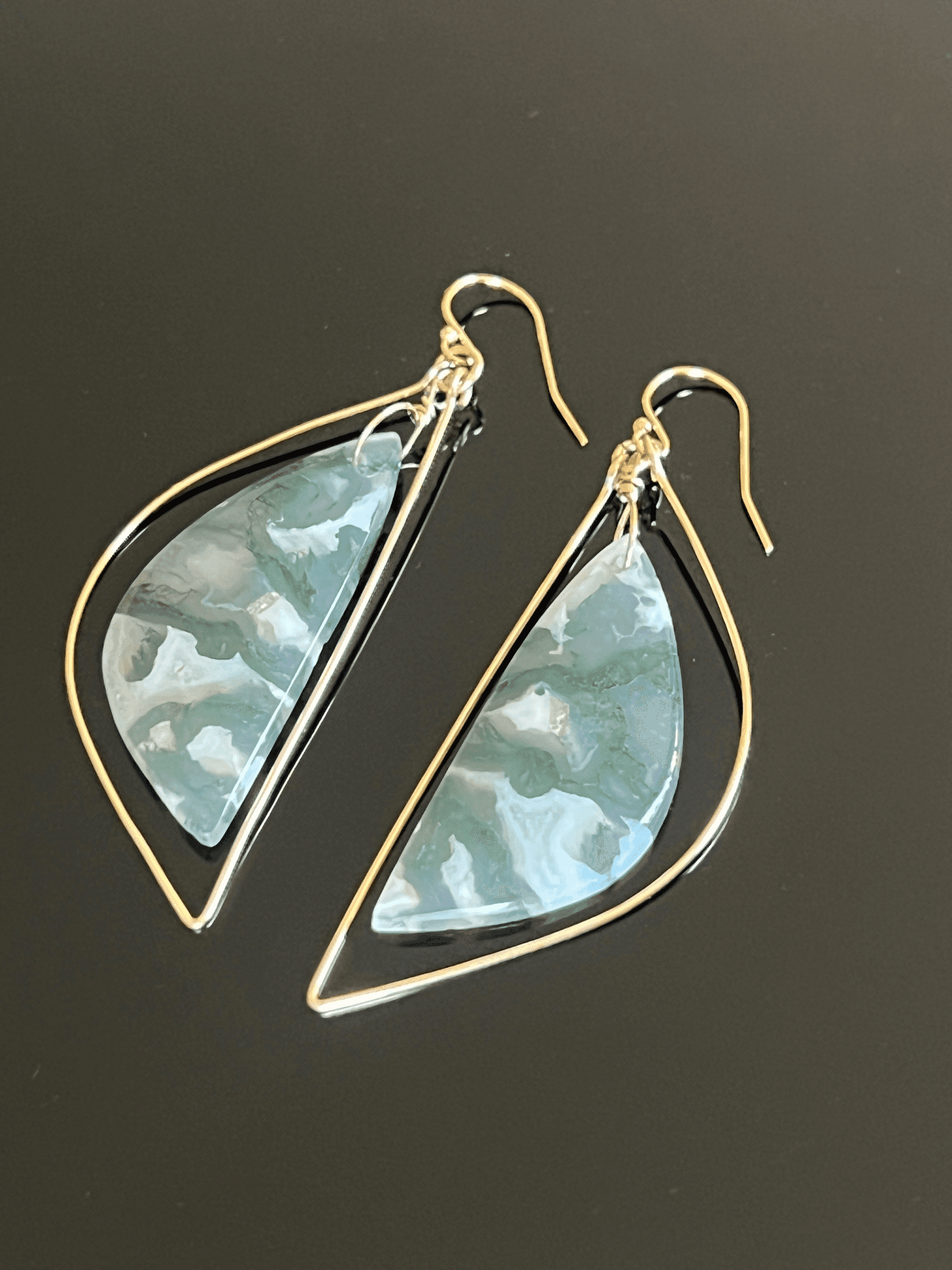 Handmade drop earrings with green patterned stones suspended inside elongated gold-toned wire frames.