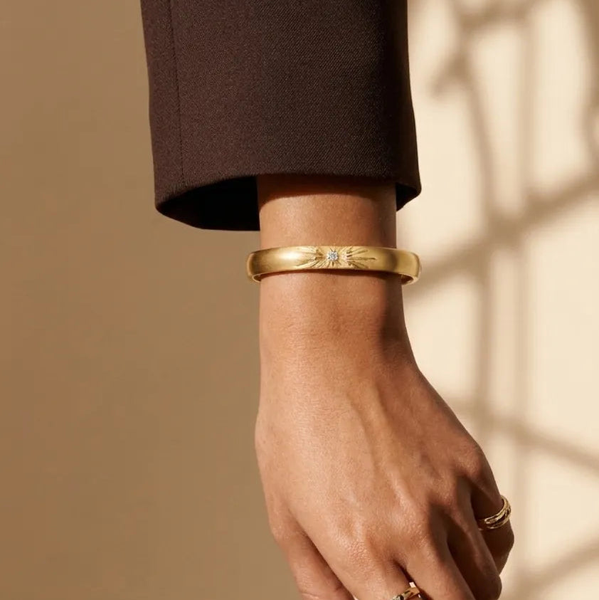 Hand wearing a gold bracelet and ring on a beige background