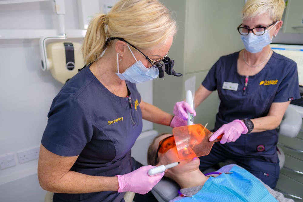 Dentist and assistant performing composite bonding treatment using a curing light and protective orange shield.