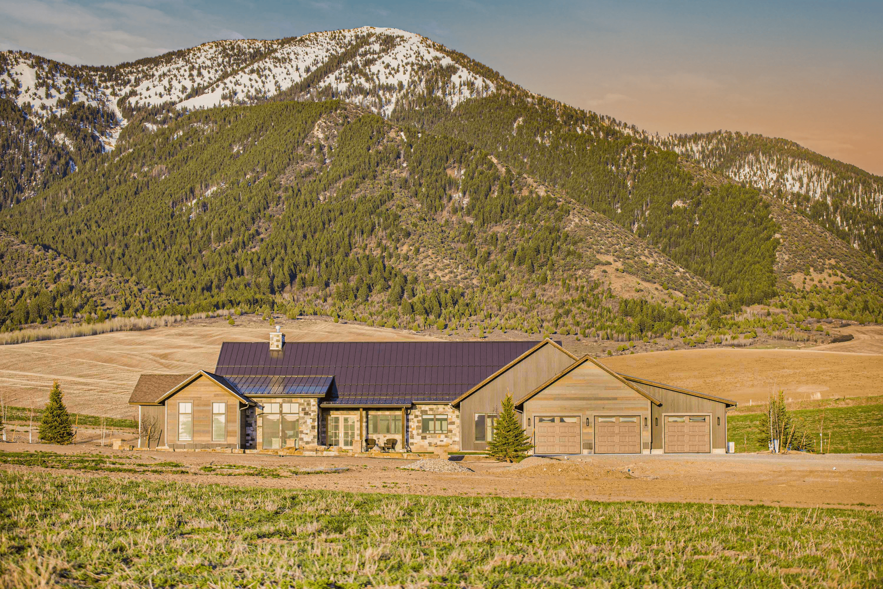 Modern home with stone and wood accents below snowy mountains.