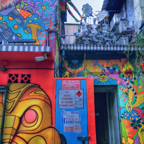 色彩缤纷的建筑外墙上覆盖着迷幻风格的壁画设计，蓝色的油箱门，以及各种警告标志。空调和植物可见。