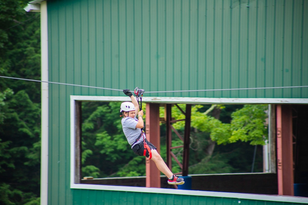 Camper riding the zipline through the trees at Camp Lenox