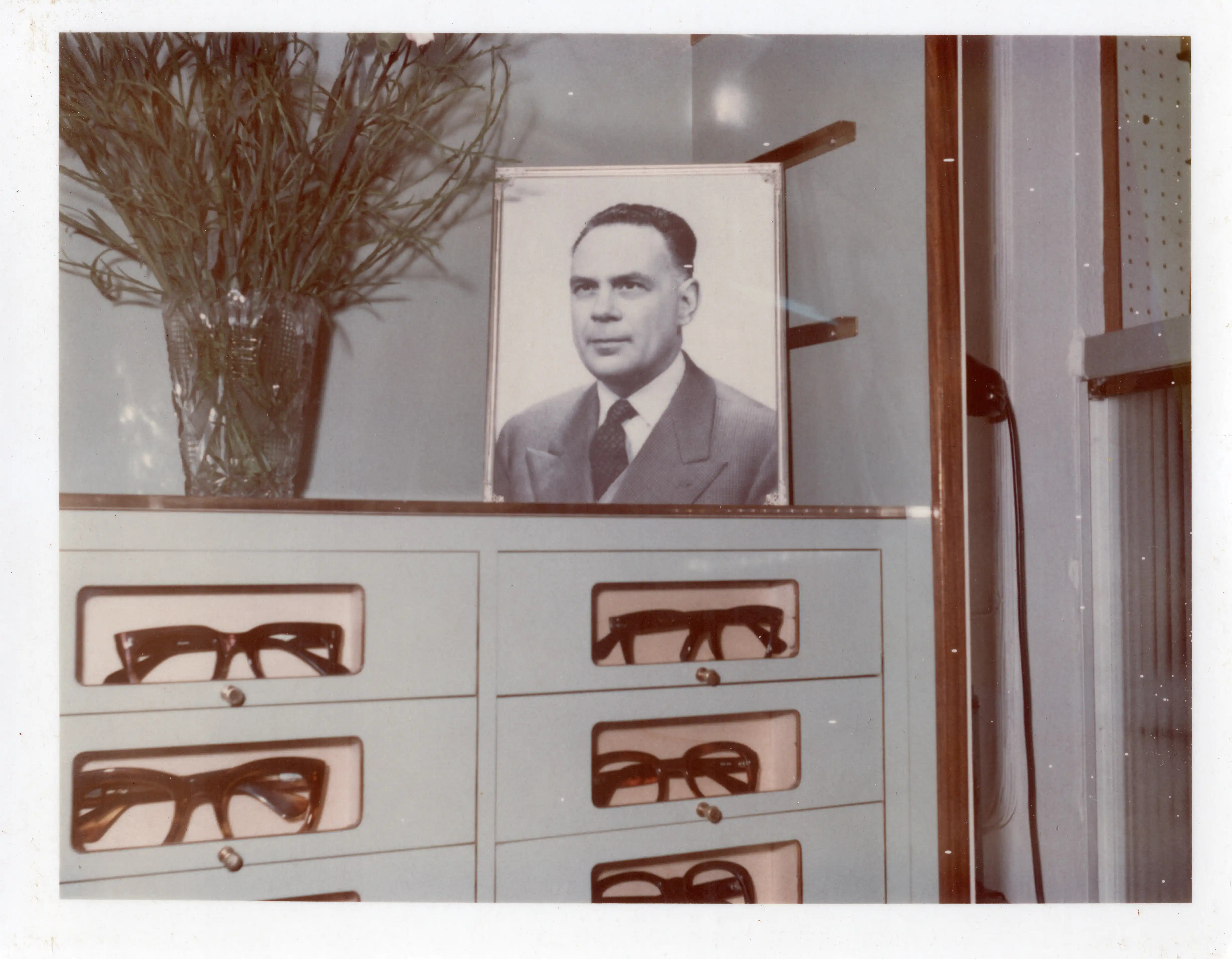 Fotografia d’archivio degli anni Cinquanta legata alla nascita di TECNOTTICA, origine dell’attuale Ottica Dentella ad Ancona, con il titolare dell’epoca ritratto all’interno dello storico negozio di ottica accanto all’esposizione di montature. L’immagine racconta l’inizio di una storia familiare cominciata nel 1956 e fondata fin dall’origine su innovazione, ricerca tecnica, qualità delle lenti oftalmiche e attenzione alla visione.