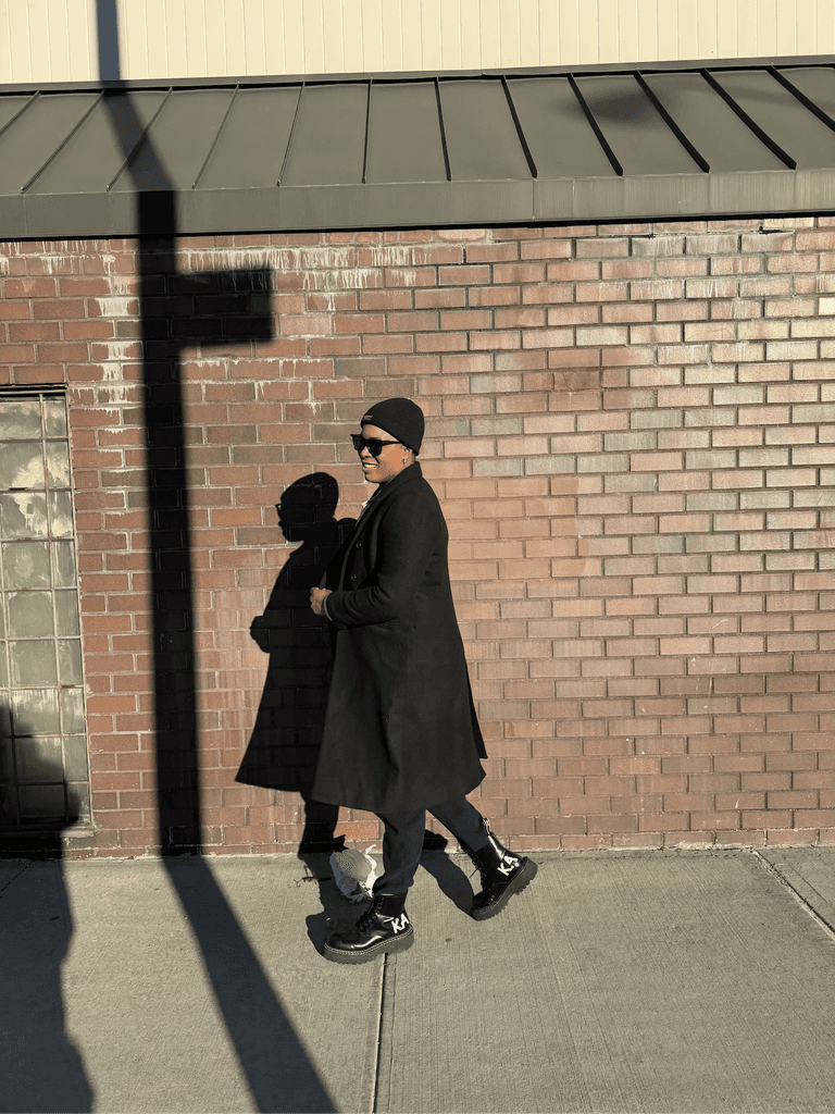 Ashleigh Warren walks closely along a brick wall, casting long shadows in the afternoon light.