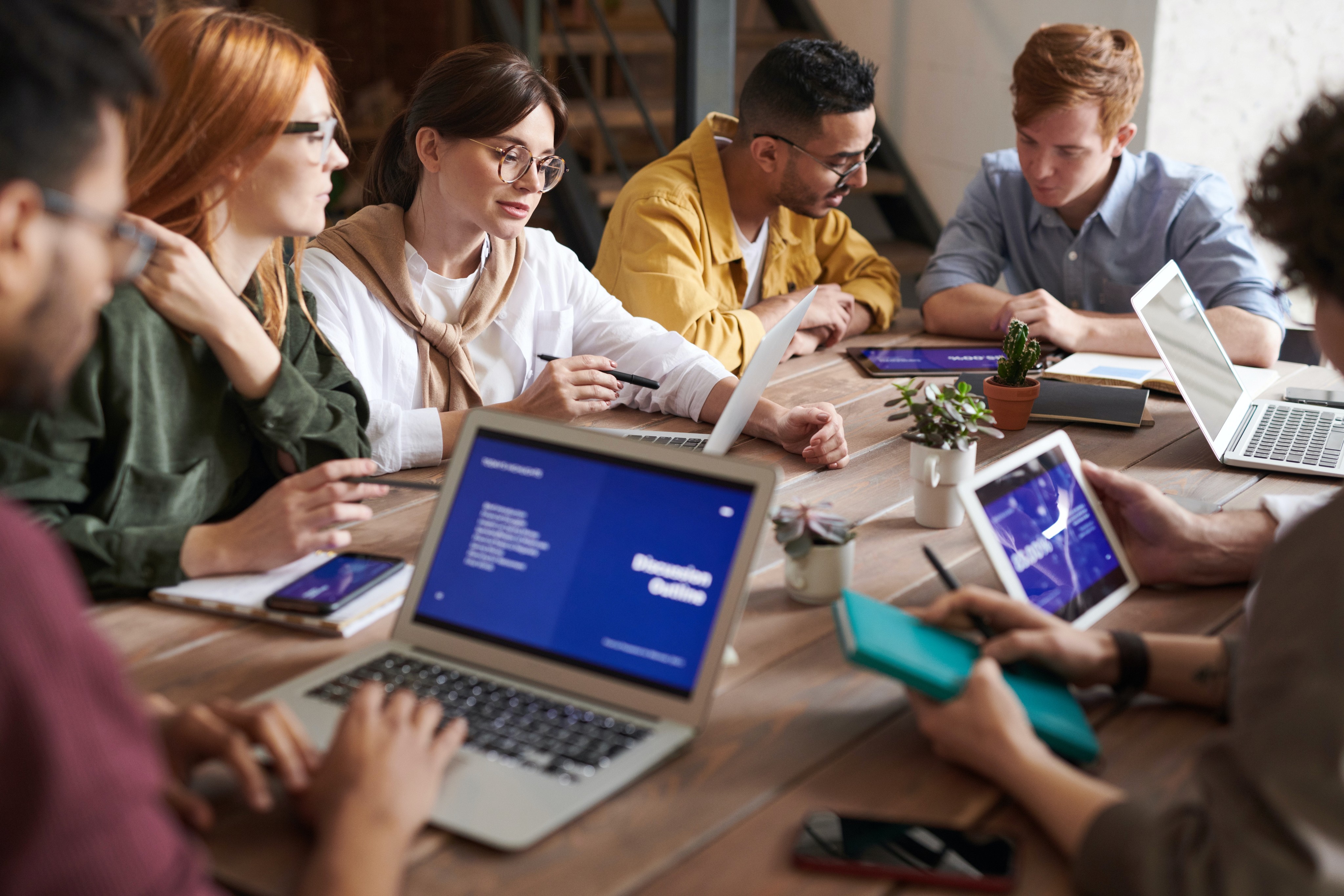 A group of people sitting around a table and working on computers.