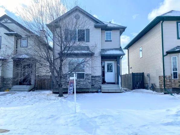 Two-story single-family home with light grey siding, stone accents, and a snow-covered yard in Scenic Acres, NW Calgary