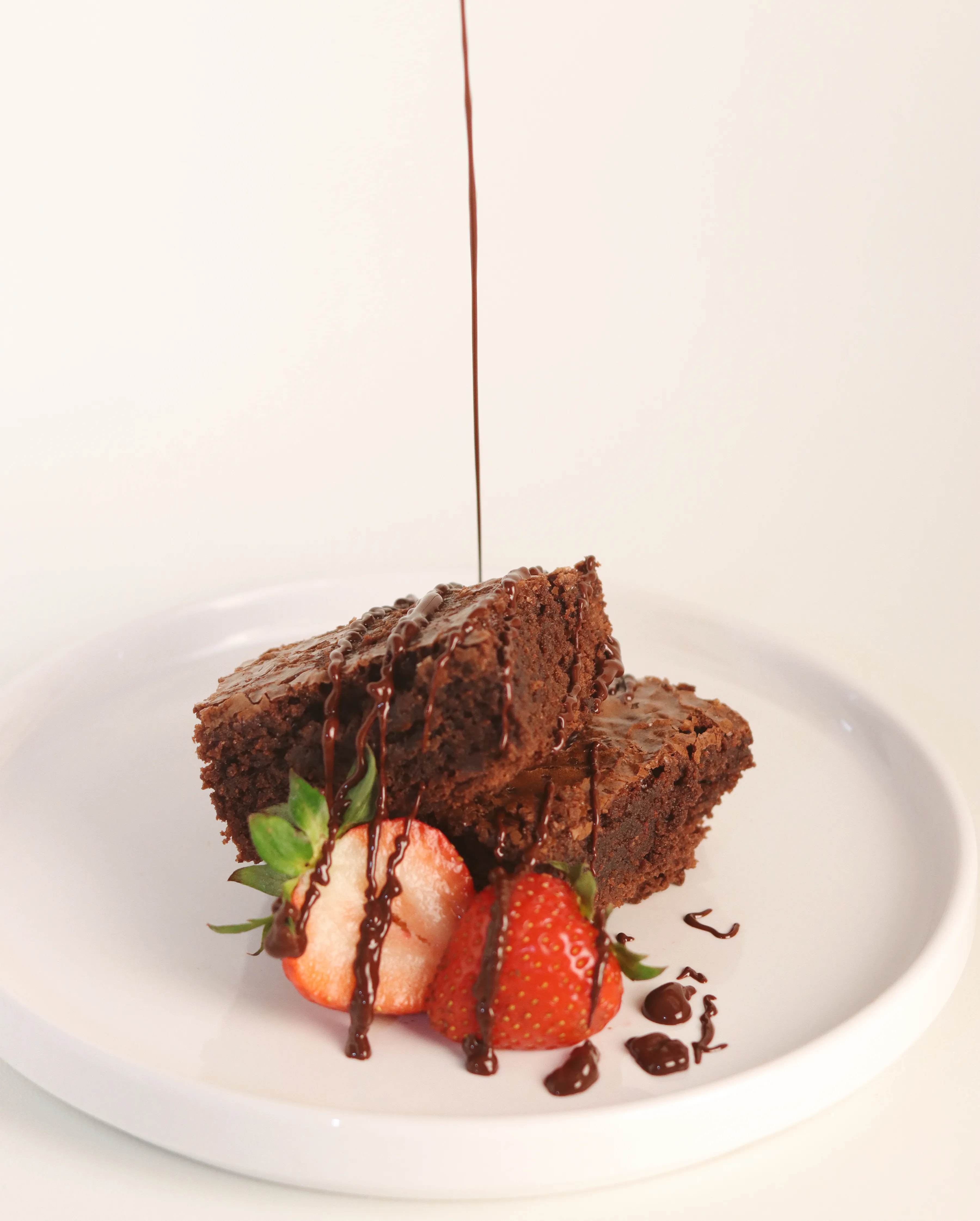 Brownie con sirope de chocolate cayendo sobre fresas