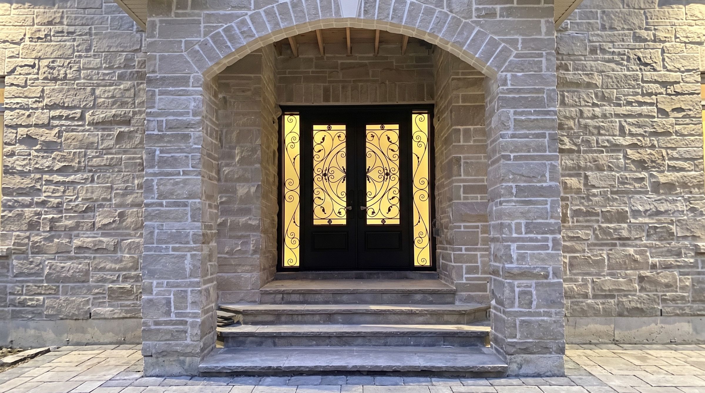 Wrought iron double front door with an arched stone surround, custom-built by Door Gallery