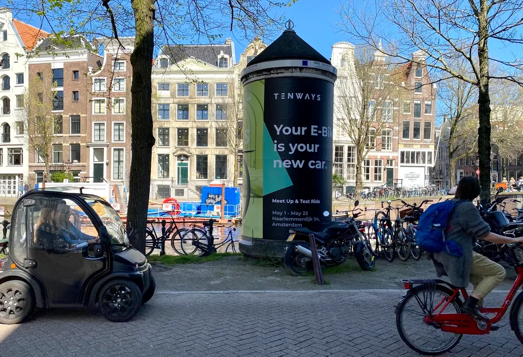 a man walking down a street past a large poster