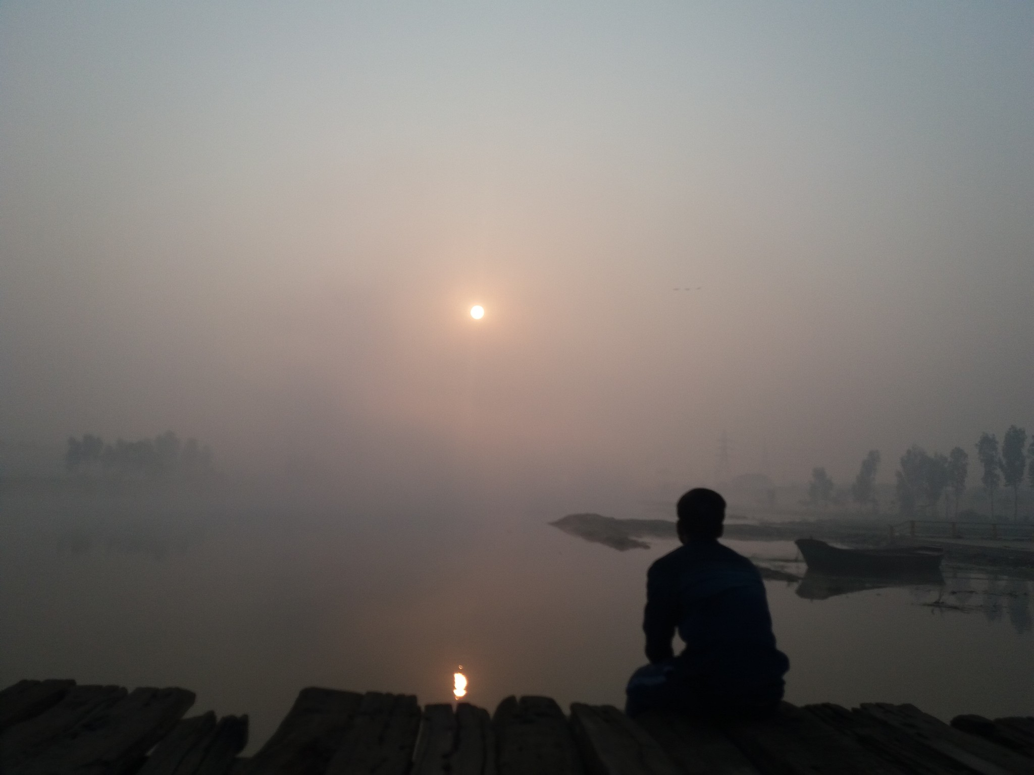 Guy sitting on a wooden bridge on a river at sunrise