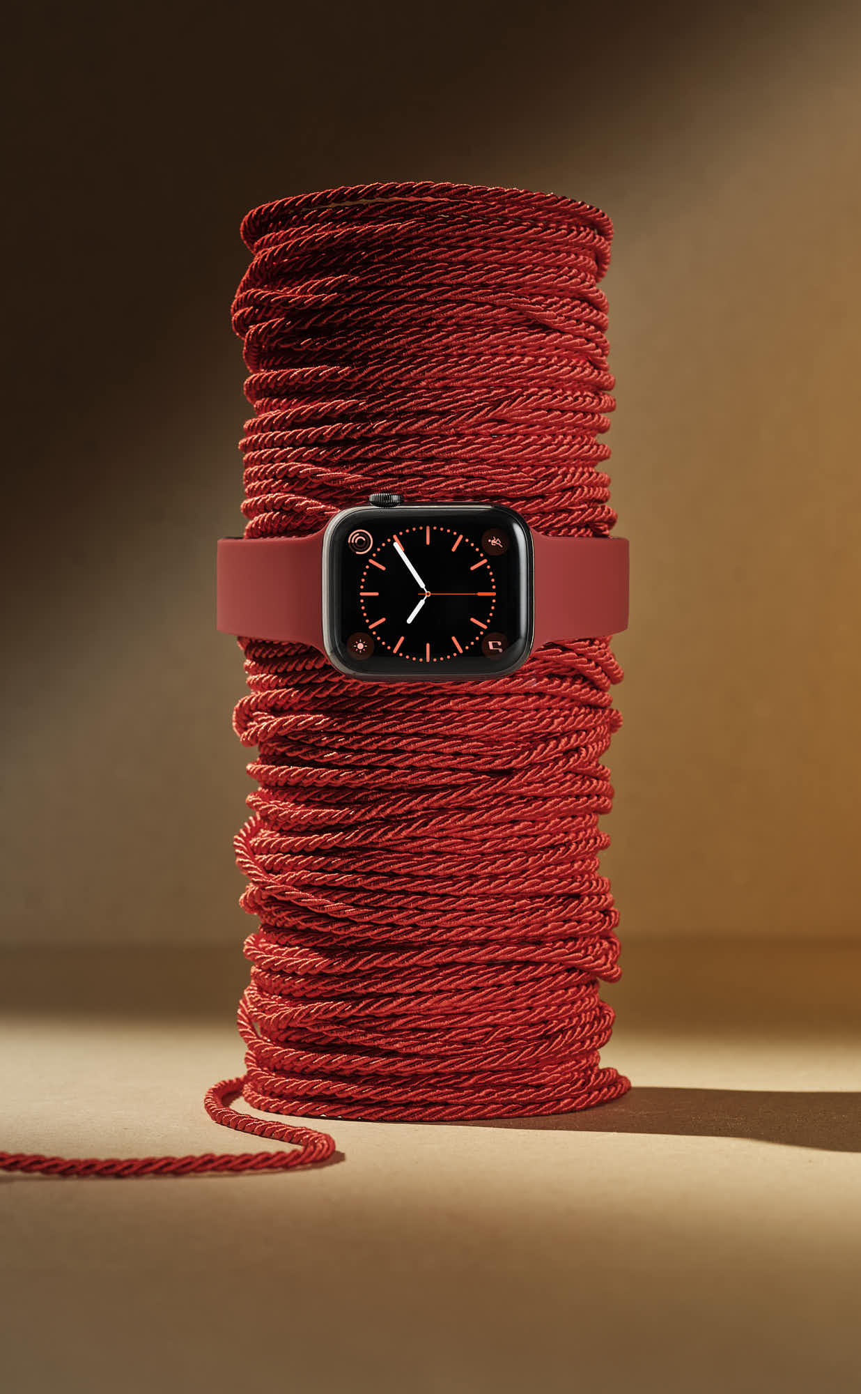 Red smartwatch wrapped around a spool of matching red rope.