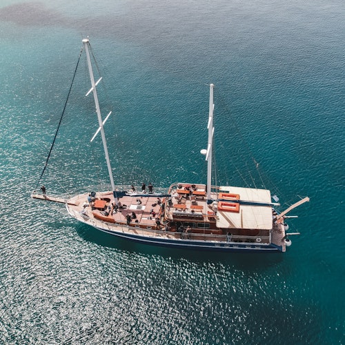 從空中俯瞰一艘擁有兩根桅杆的帆船，停泊在清澈的碧綠水域中，甲板和設備清晰可見。