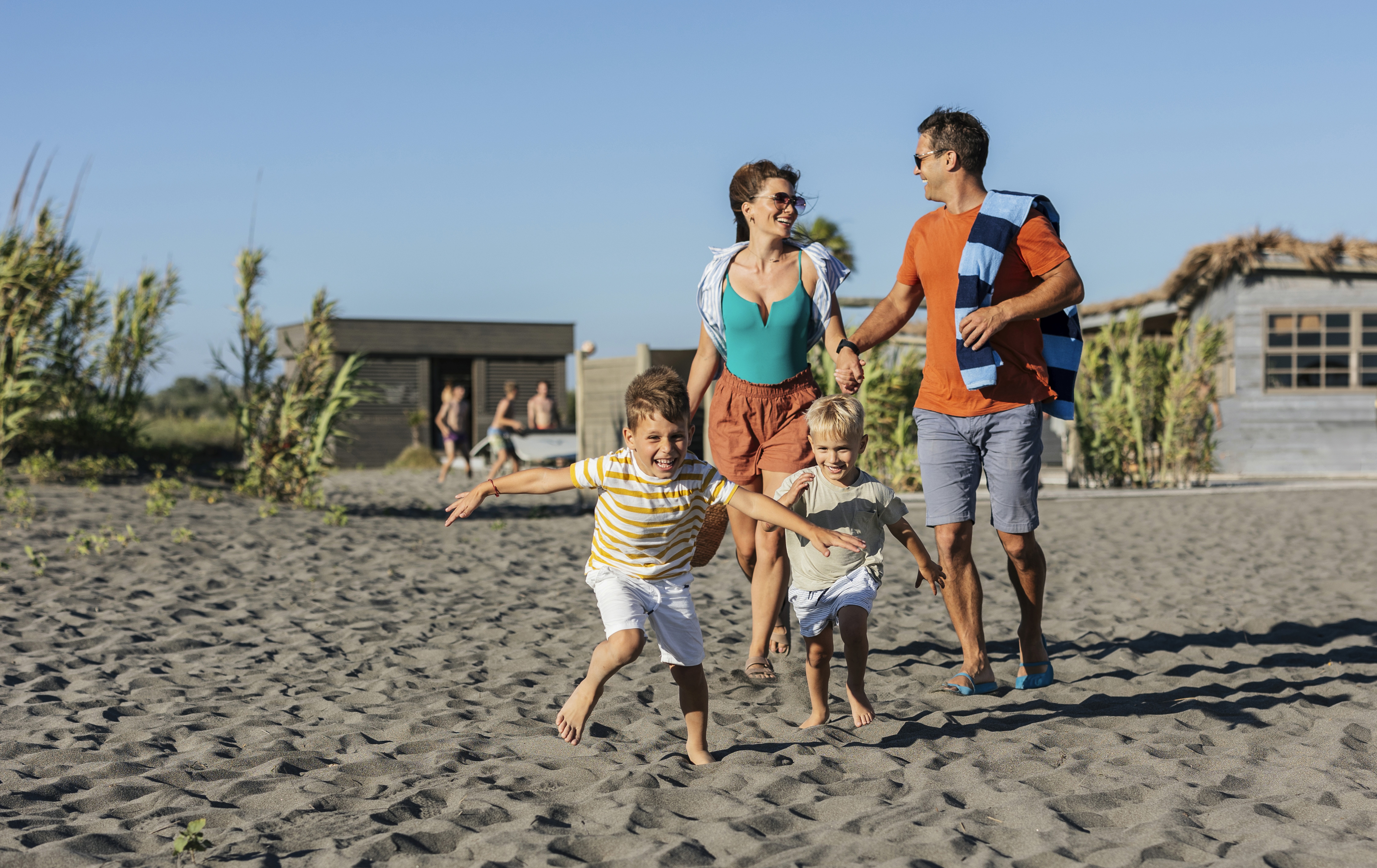 Familie läuft gemeinsam mit zwei Kindern barfuß über den Strand im Urlaub.