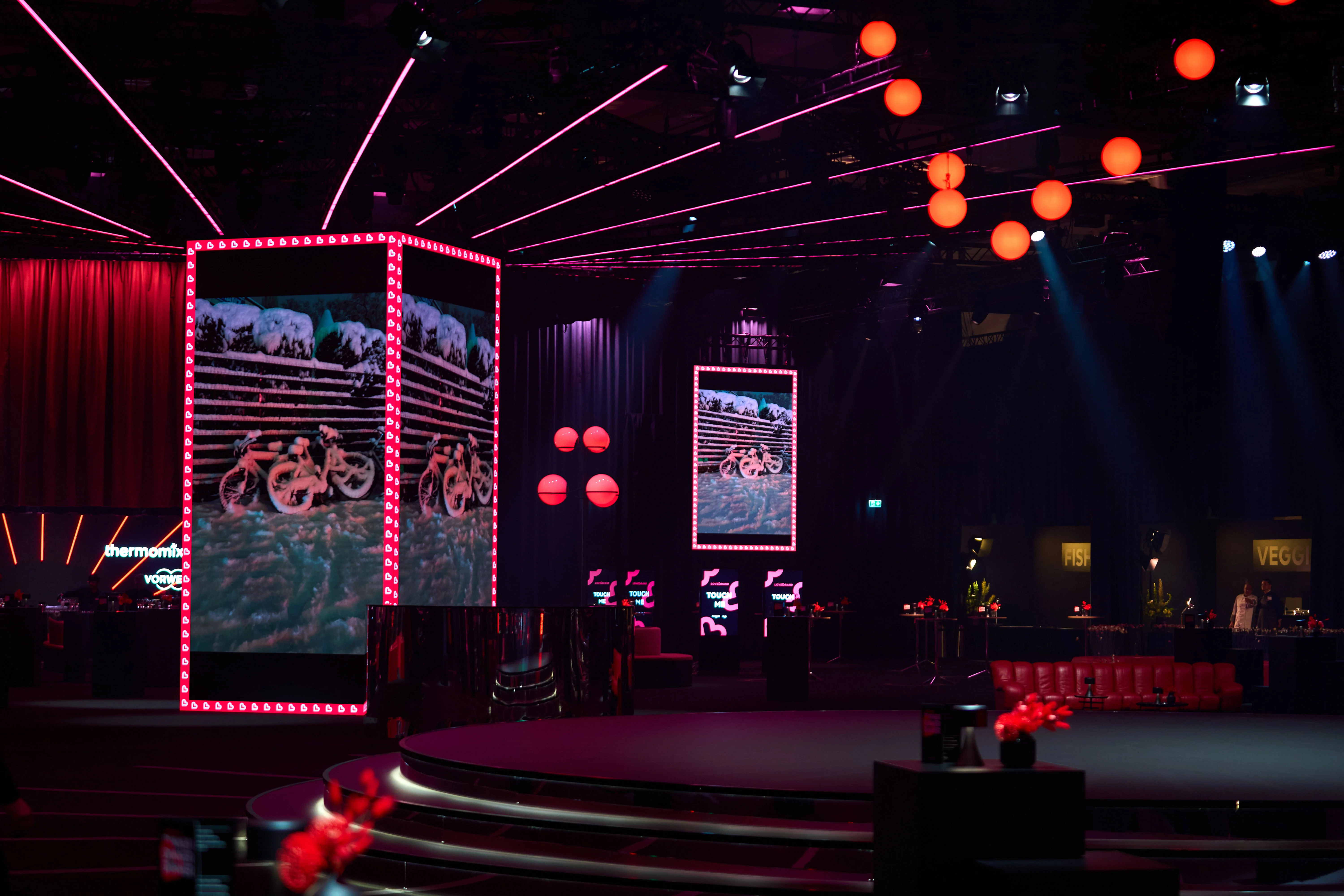 LED screen pillars with light bulb frames and red spheres around the dark stage.
