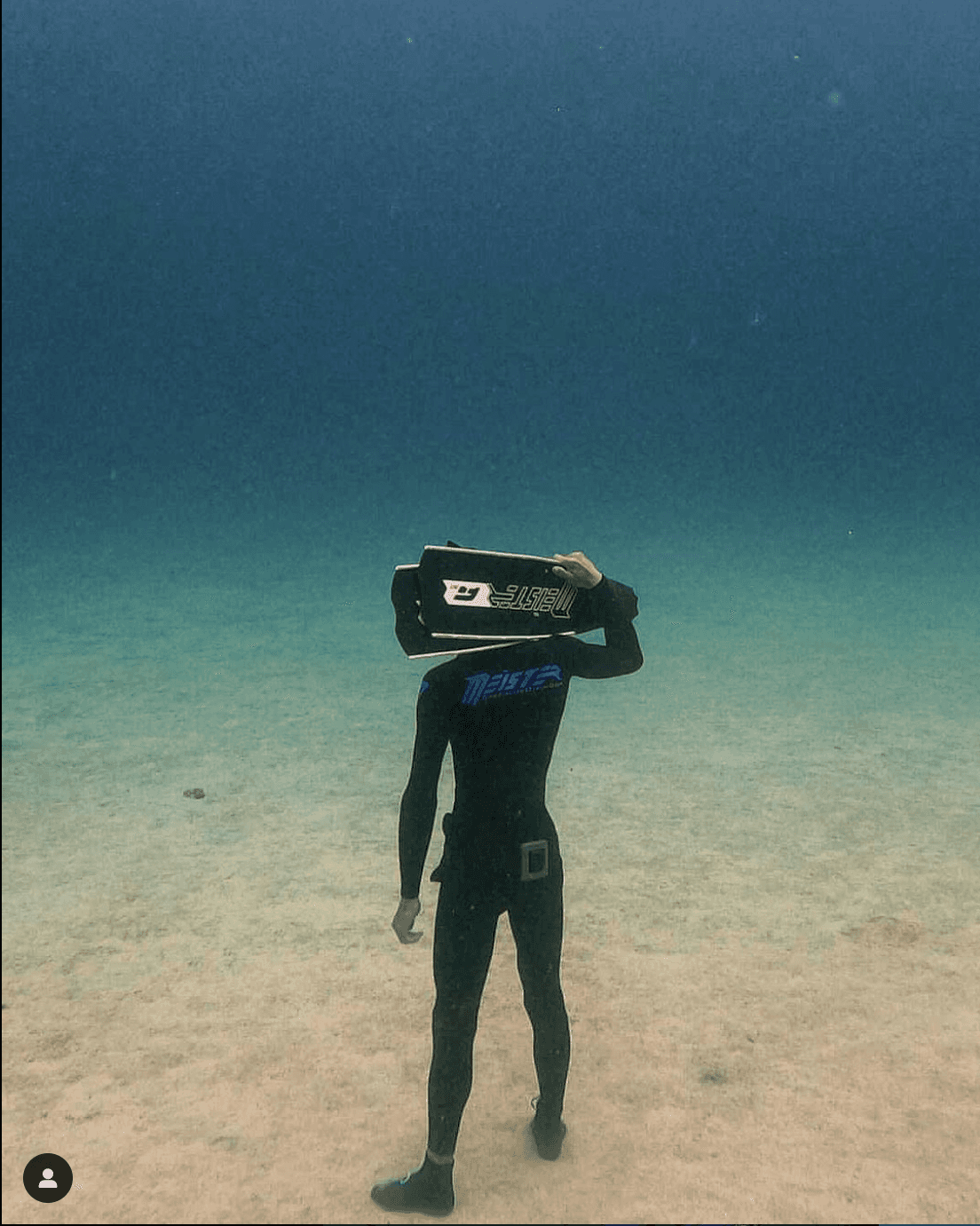 freediver meister holding fins standing underwater