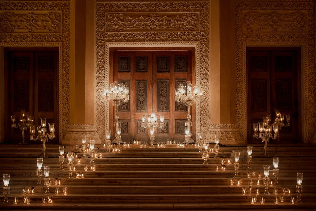 Landscape with a vineyard in rows leading to a building with a tower, rolling hills in the distance.