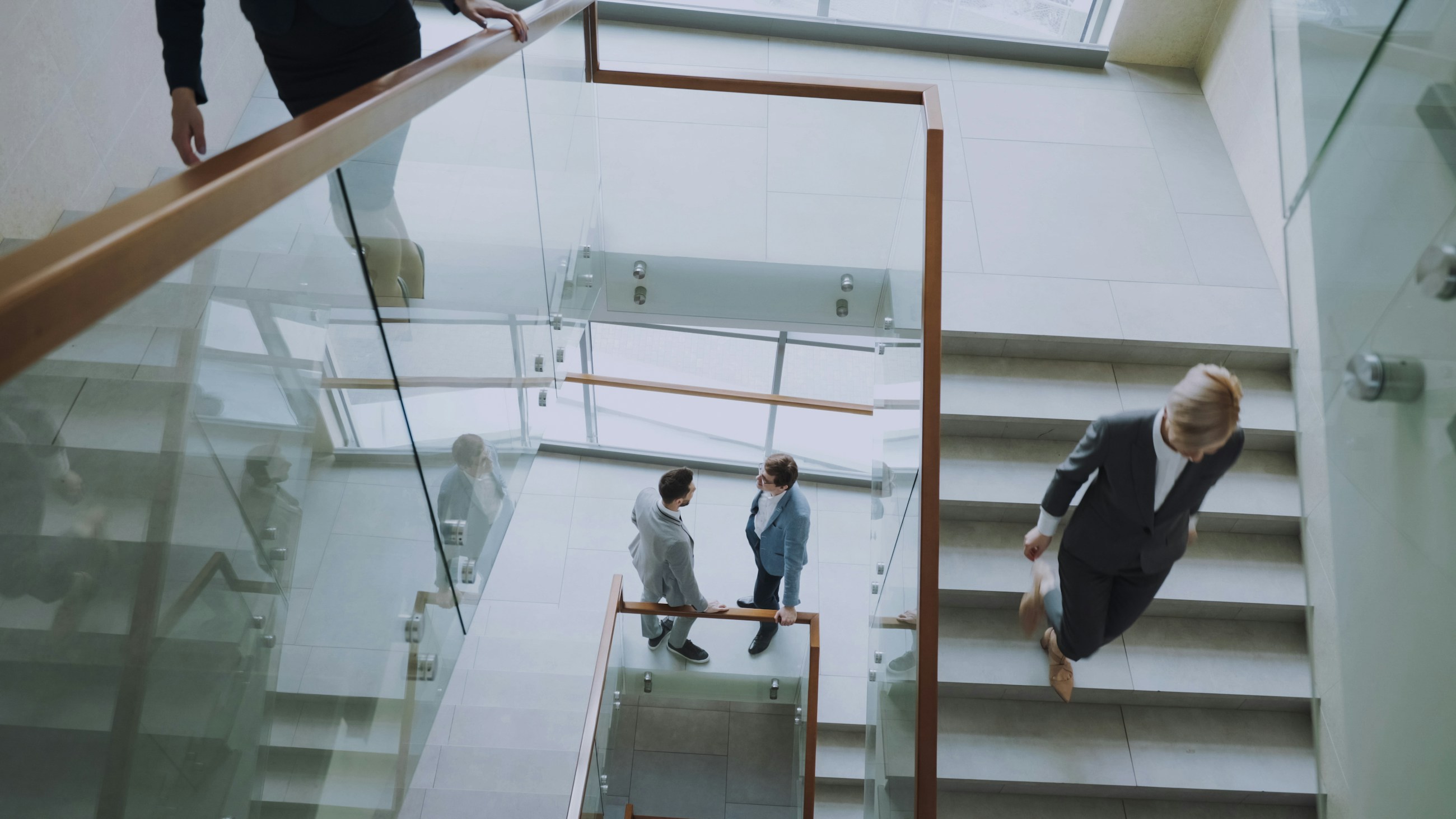 People walking on stairs and standing on a shared landing in a glazed interior; illustrative photography, not verified KEYCO project work
