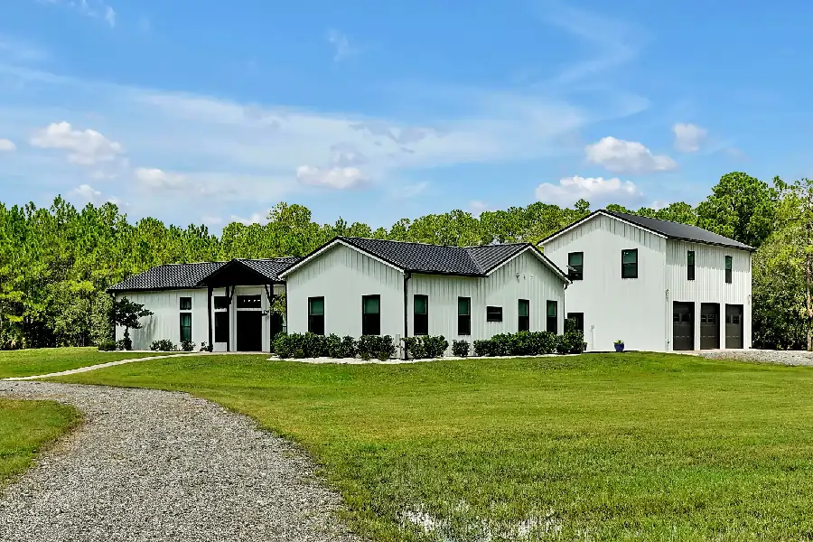 A white home featuring a driveway, set against a backdrop of a lush grassy field.