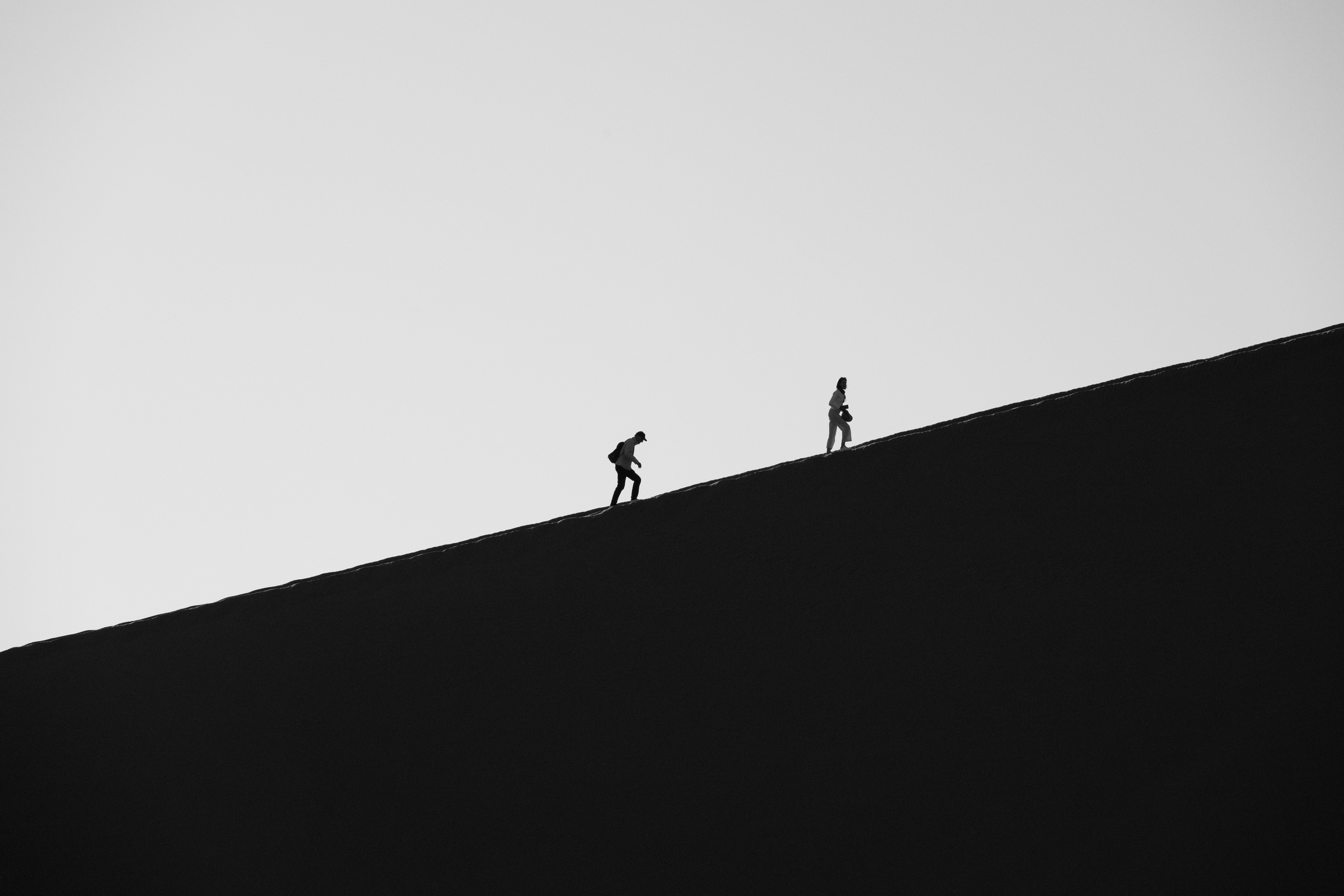 Two hikers ascend a dark, barren dune.