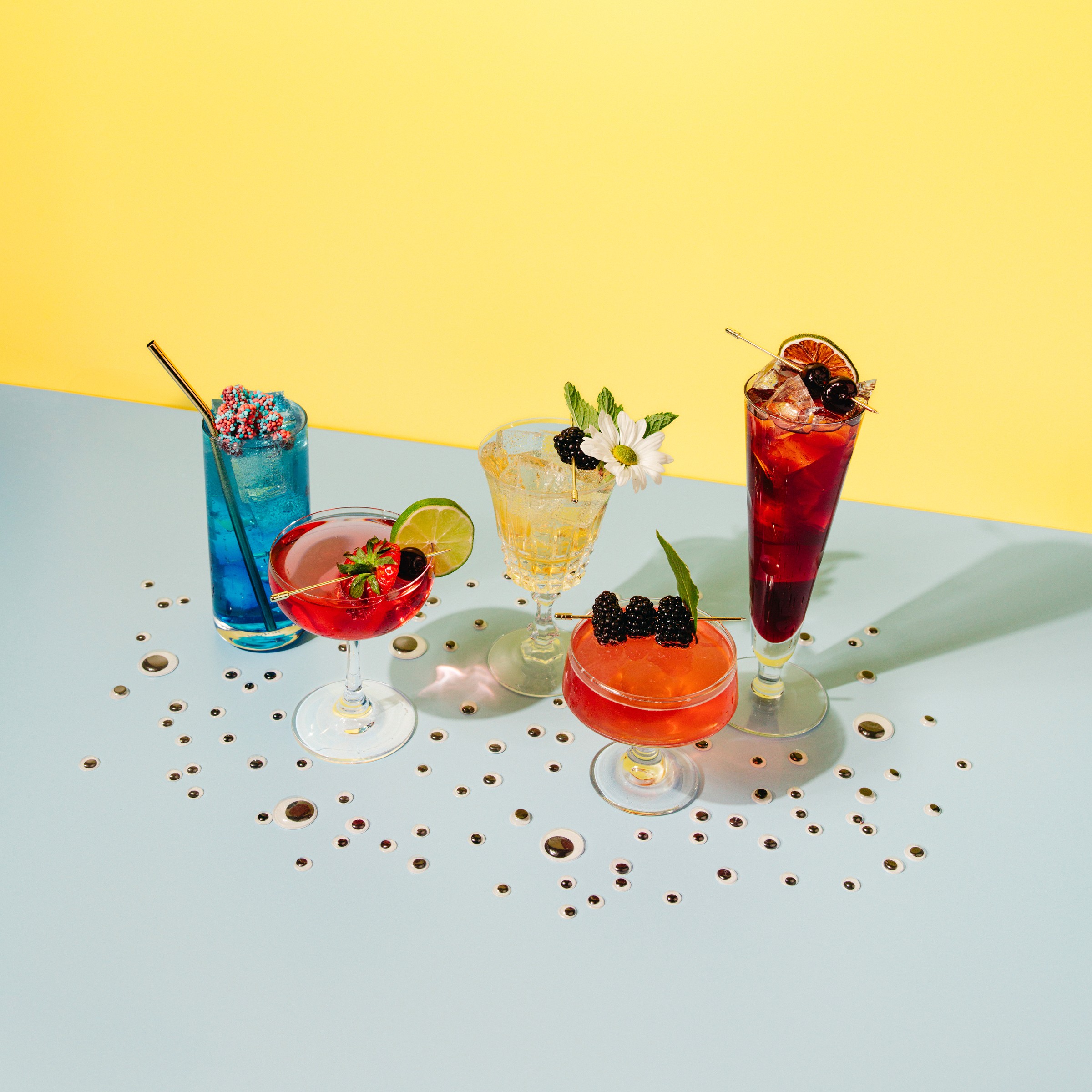 Collection of five curiously vibrant non-alcoholic drinks with googly eyes scattered around