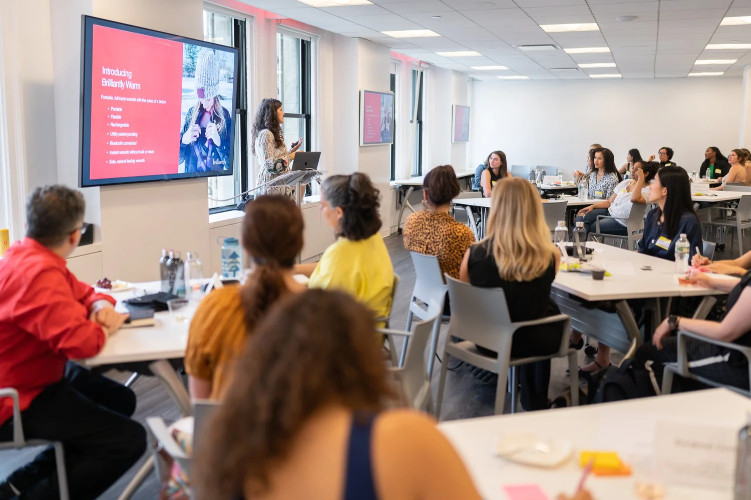 Groups of people sitting around desks while a speaker presents