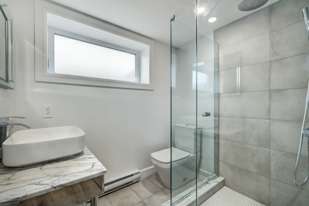 Stylish condo bathroom update with oversized grey tile shower, frameless glass enclosure, and marble countertop vanity, reflecting B&Y Reno Corp’s upscale finishes in smaller spaces