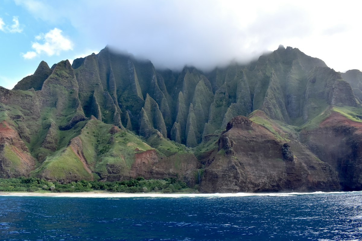 Jagged green cliffs of the Napali Coast on Kauai rising above deep blue ocean under low clouds