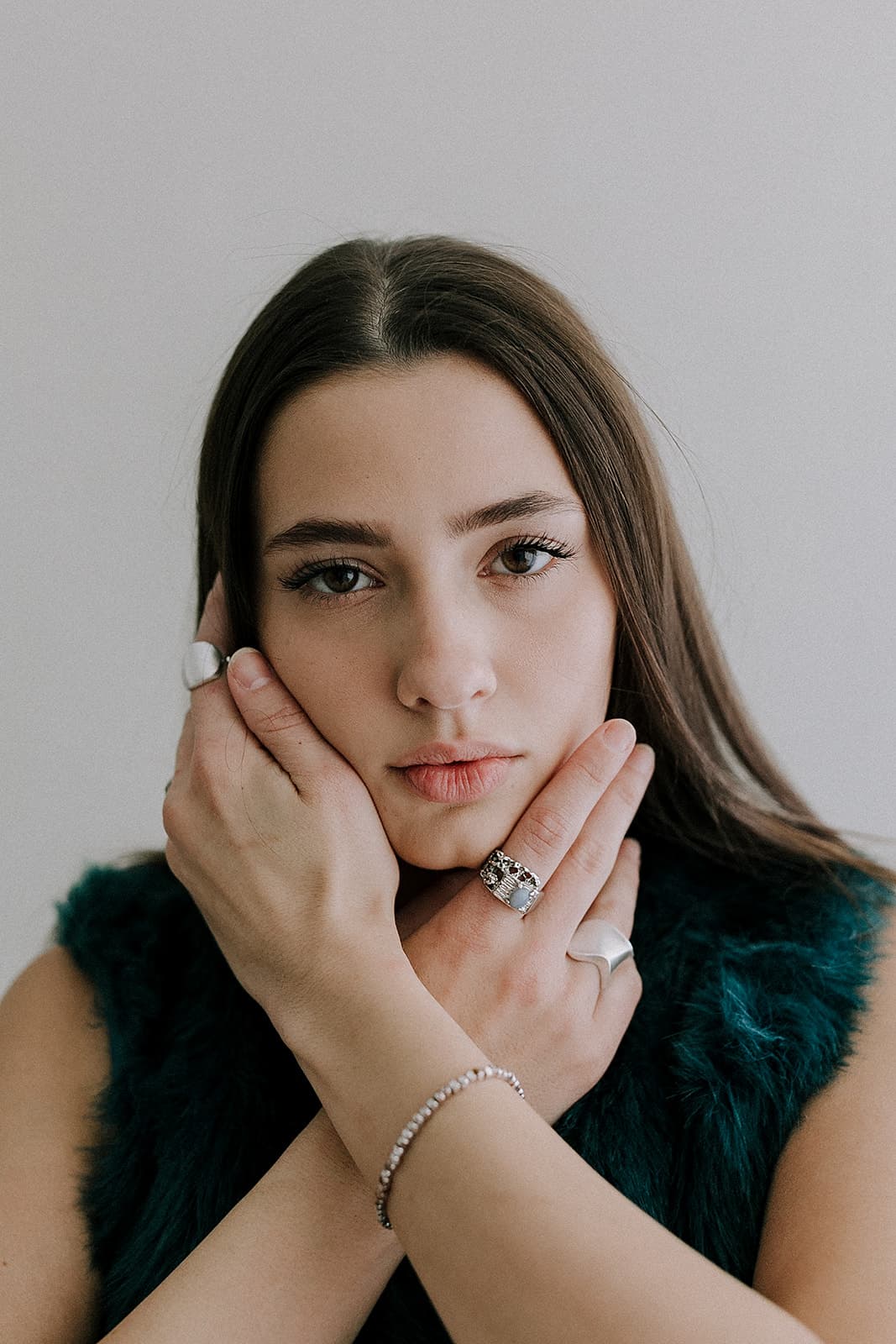 A close-up portrait of a model cradling her face with her hands, taken in the natural light at Revelator Studio, a Shreveport-based photography studio.