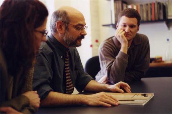 A photo of three people siting at a table and looking at some notes.
