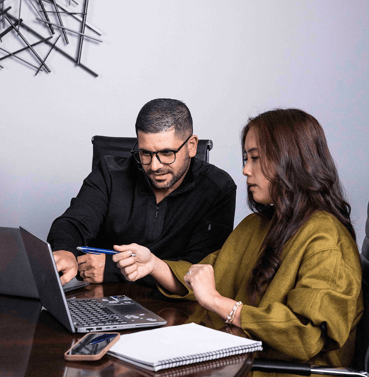 Two business professionals collaborating at a office table while reviewing data on a laptop.