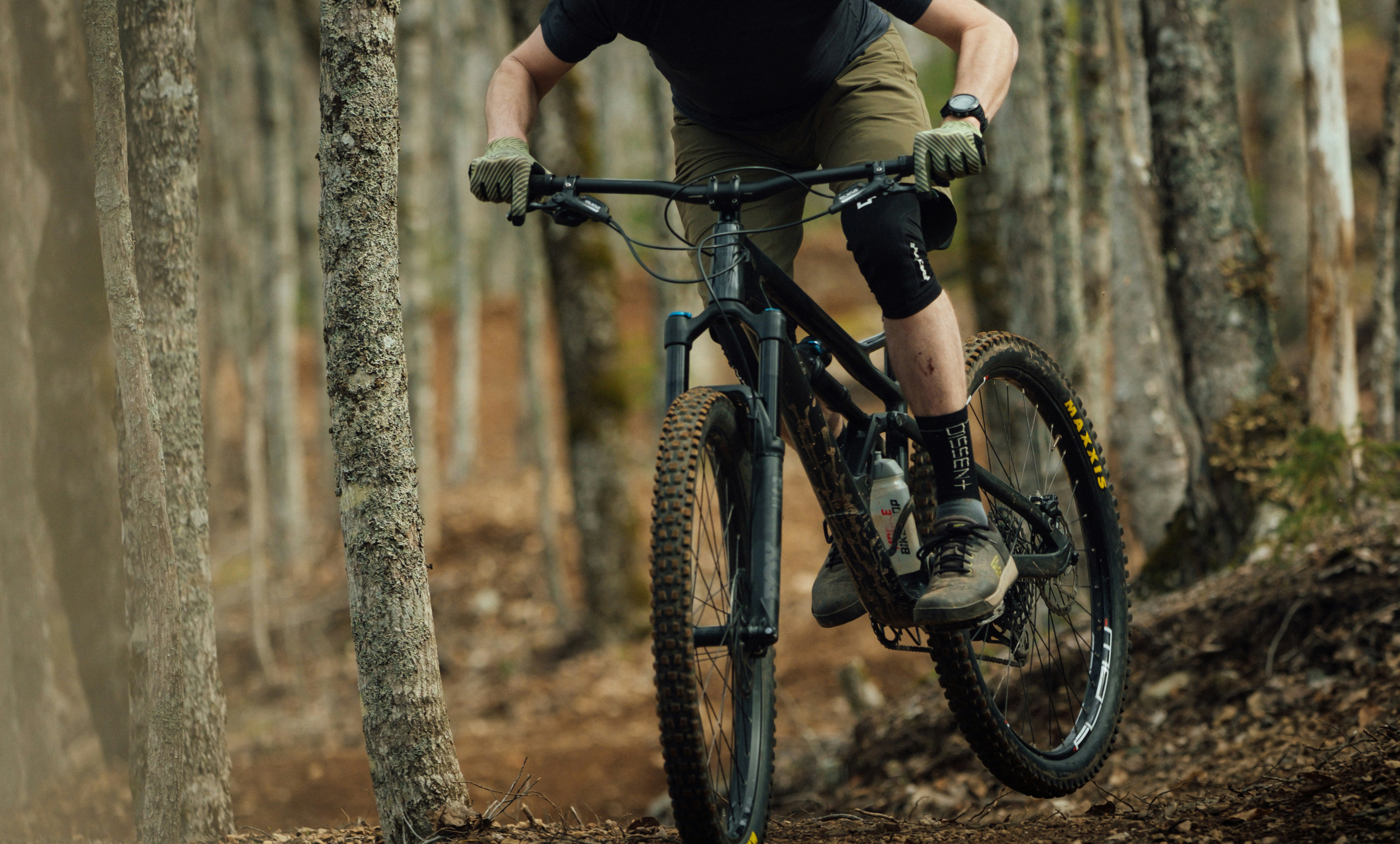 Vététiste sur un vélo tout-terrain tout-suspendu dévalant un sentier technique en forêt jonché de racines.